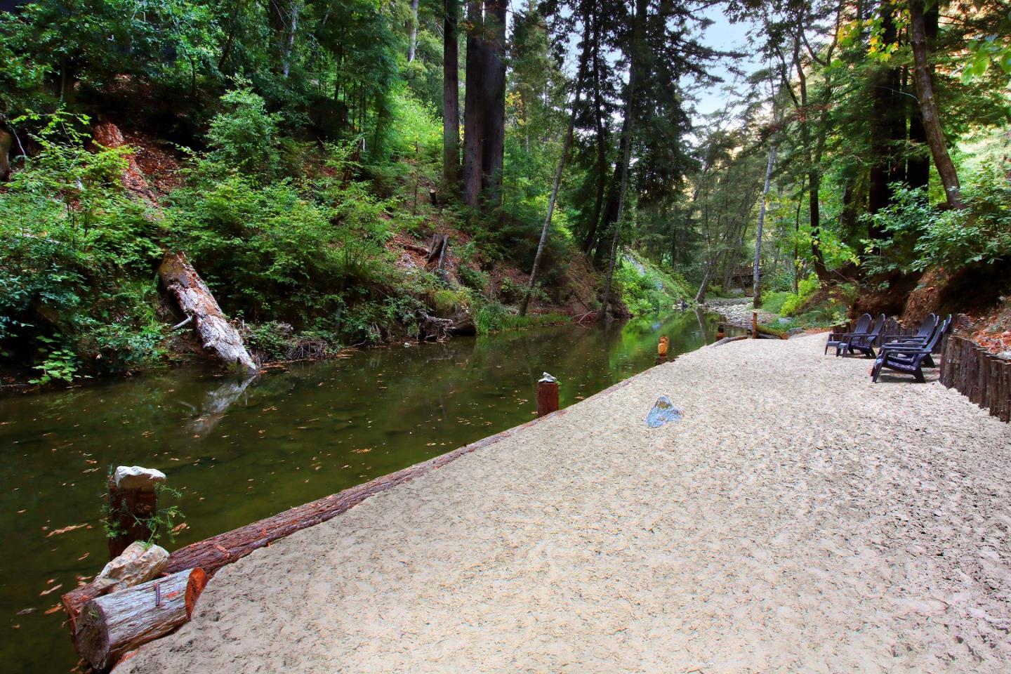 Wooded creek beside a broad gravel bank lined with Adirondack chairs.