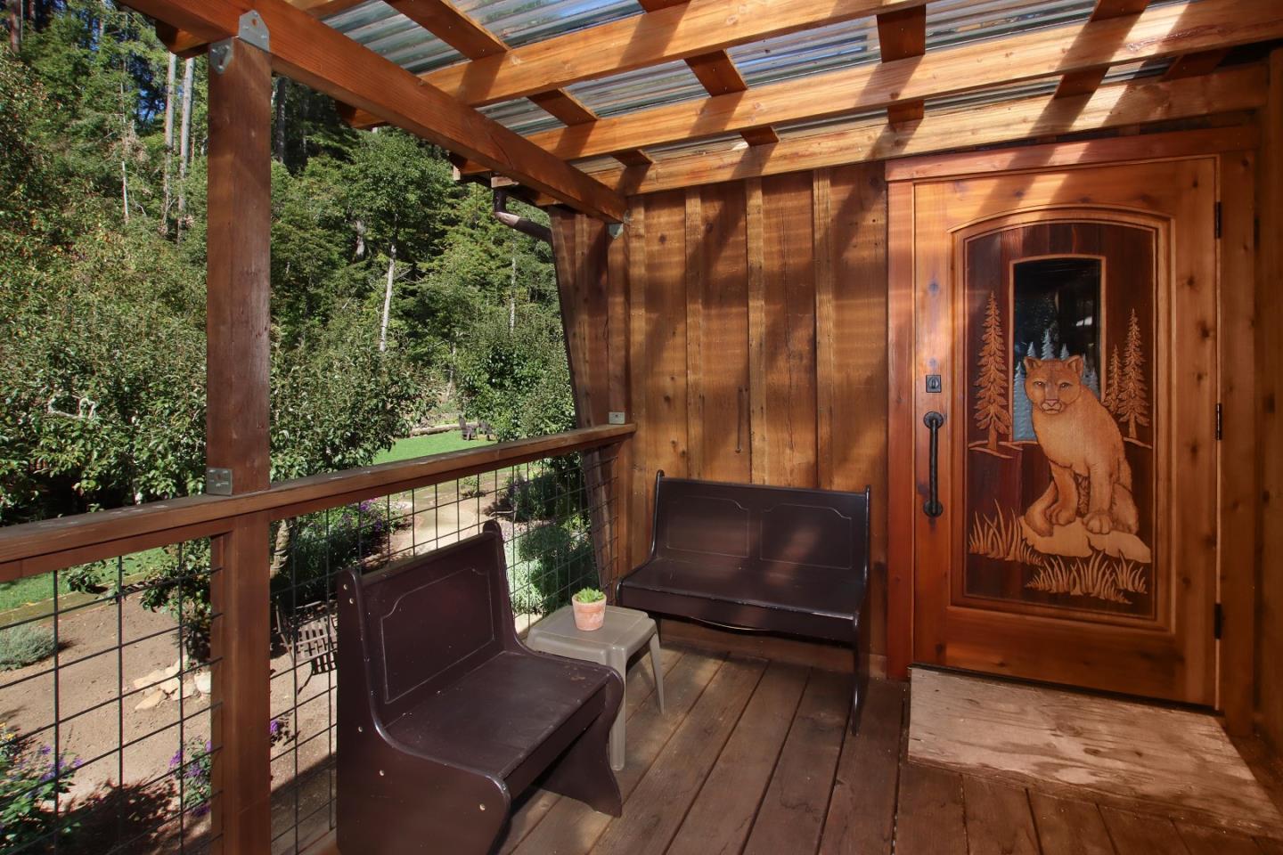 Covered wooden porch with seating and a carved cougar entry door overlooking trees.
