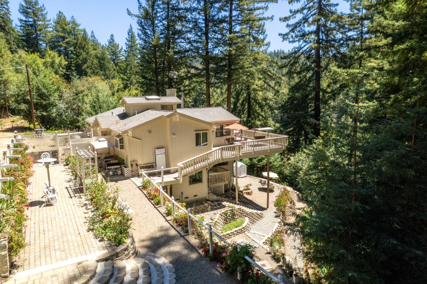 Mountain home surrounded by tall trees, with a broad raised deck and landscaped patios.