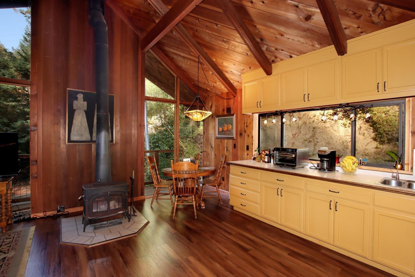 Kitchen with yellow cabinets, vaulted wood ceiling, freestanding stove, and dining nook beside a tree-lined window.