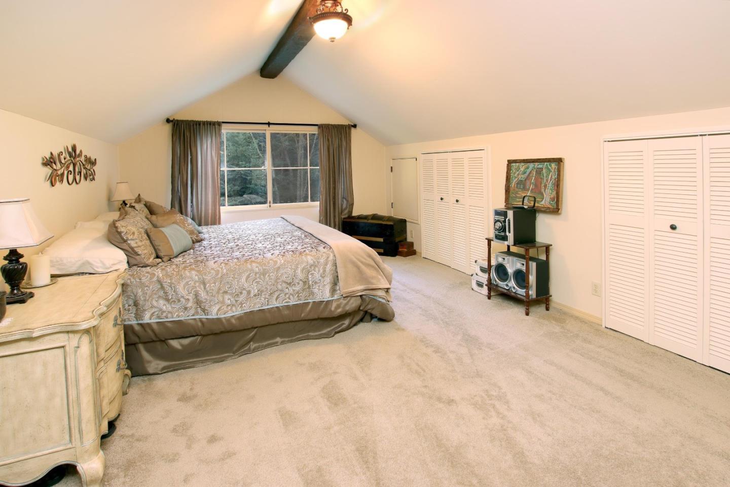 Furnished bedroom with a large bed, vaulted ceiling, and a window overlooking trees.