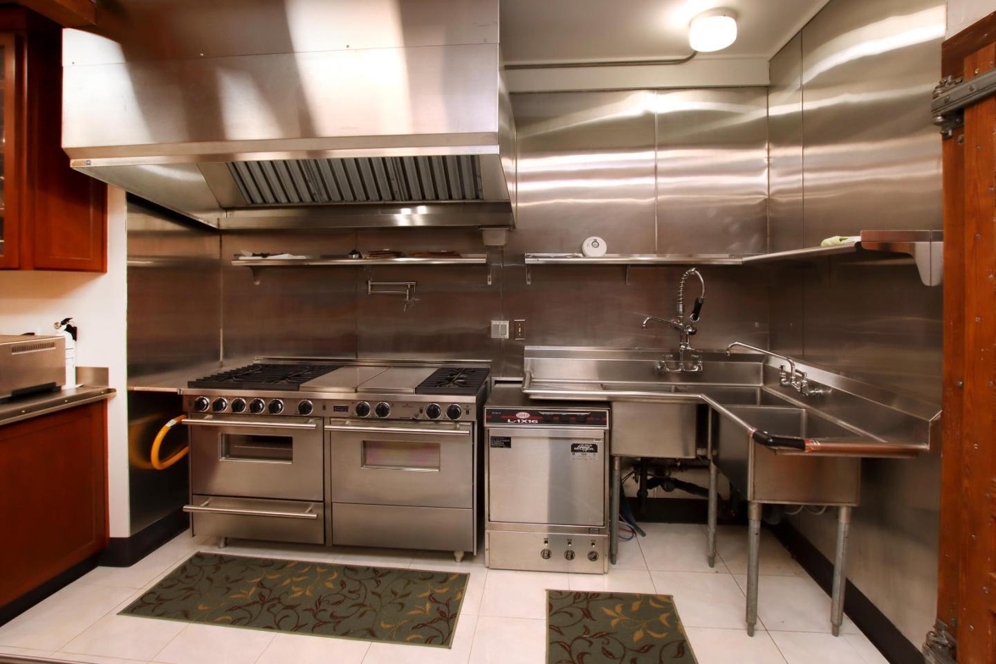Commercial-style kitchen with a stainless range, oversized hood, and deep stainless steel sink.