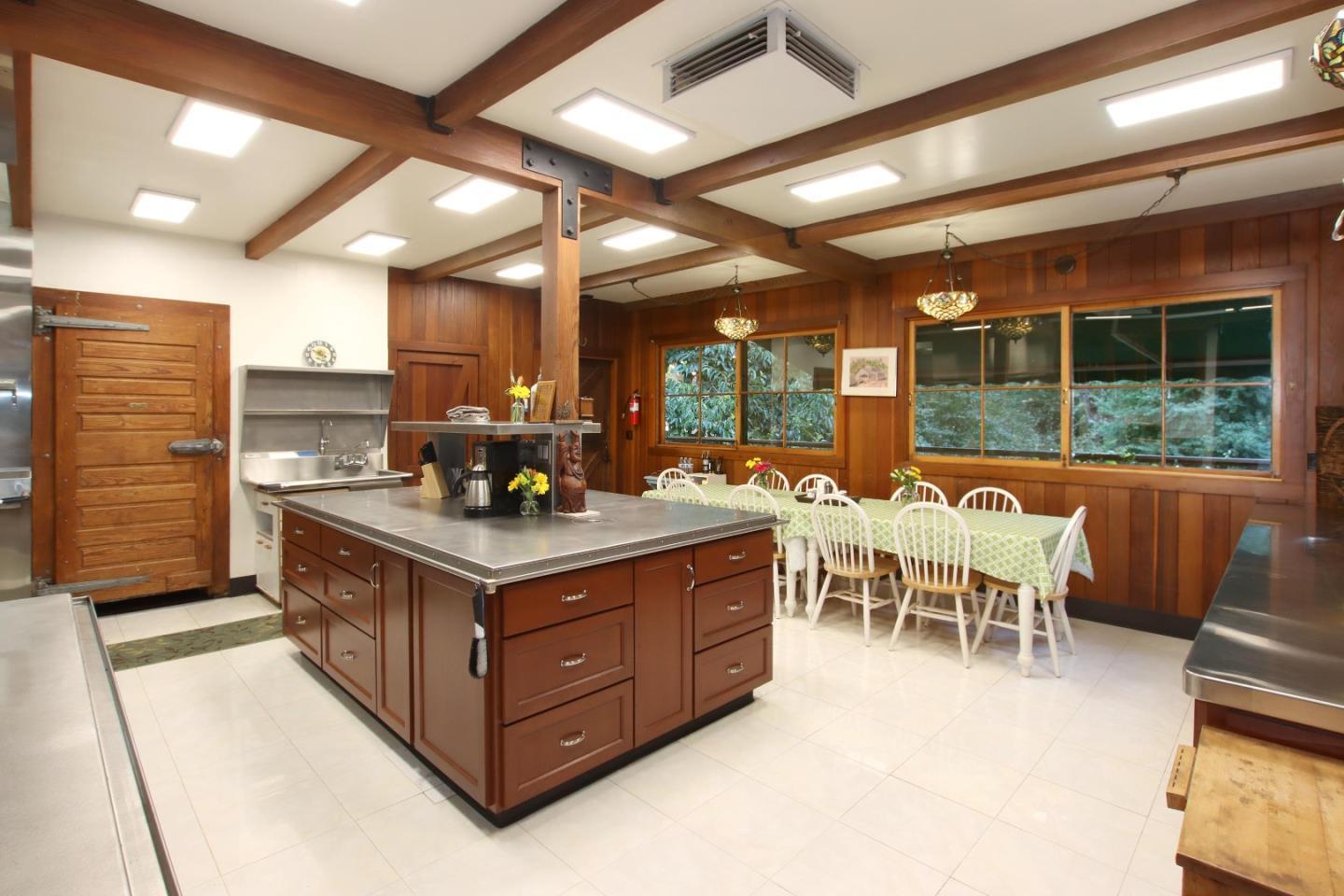 Kitchen with a large island, wood-paneled walls, exposed beams, and an adjoining dining table.