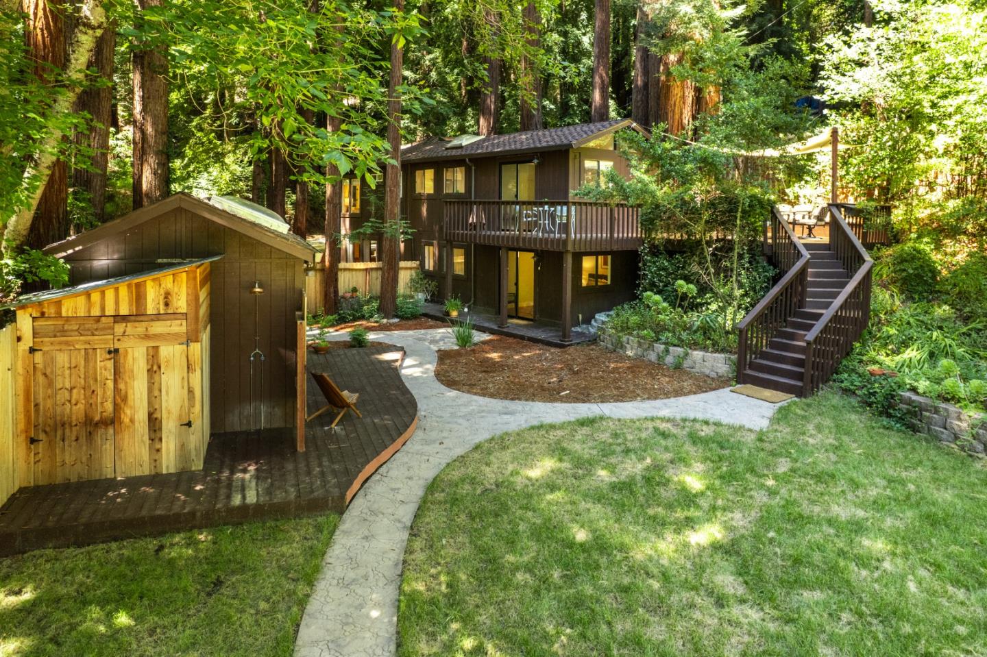 Two-story wood home among redwoods, with a curved stone path and raised deck stairs.