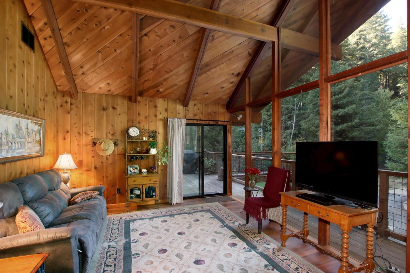 Wood-paneled living room with a vaulted ceiling and large windows overlooking trees.